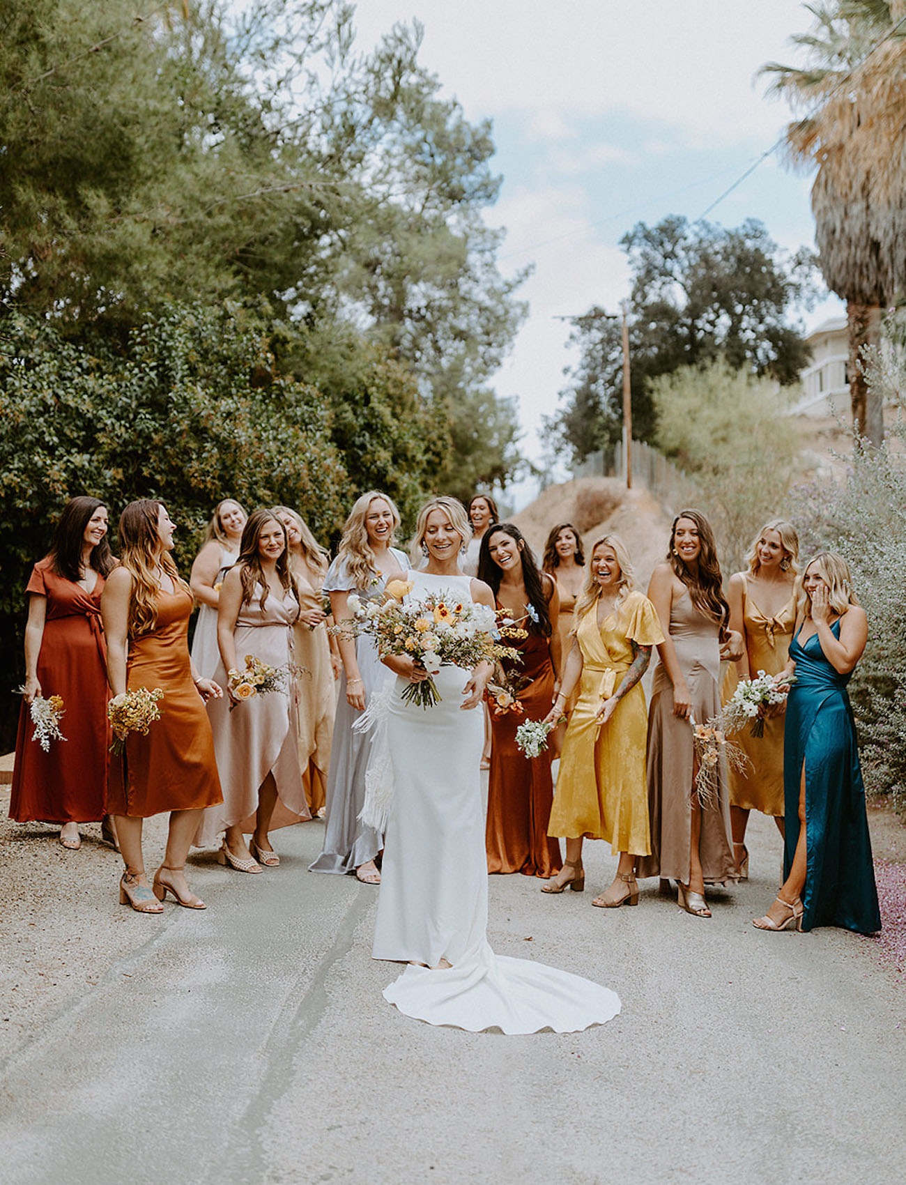 bridal party walking down a road with the bride while wearing colorful bridesmaid dresses ordered online